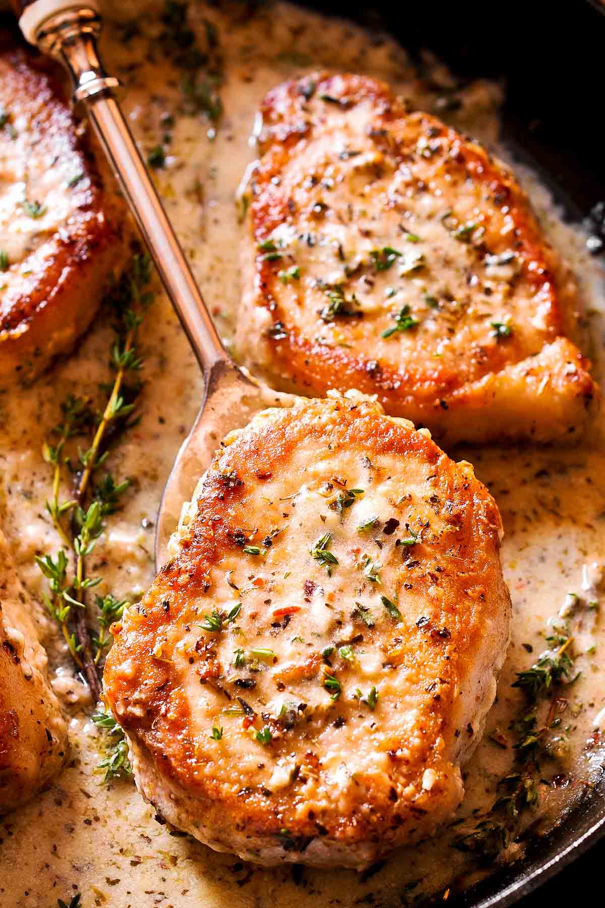 creamy pork chops in white wine sauce in skillet with thyme garnish