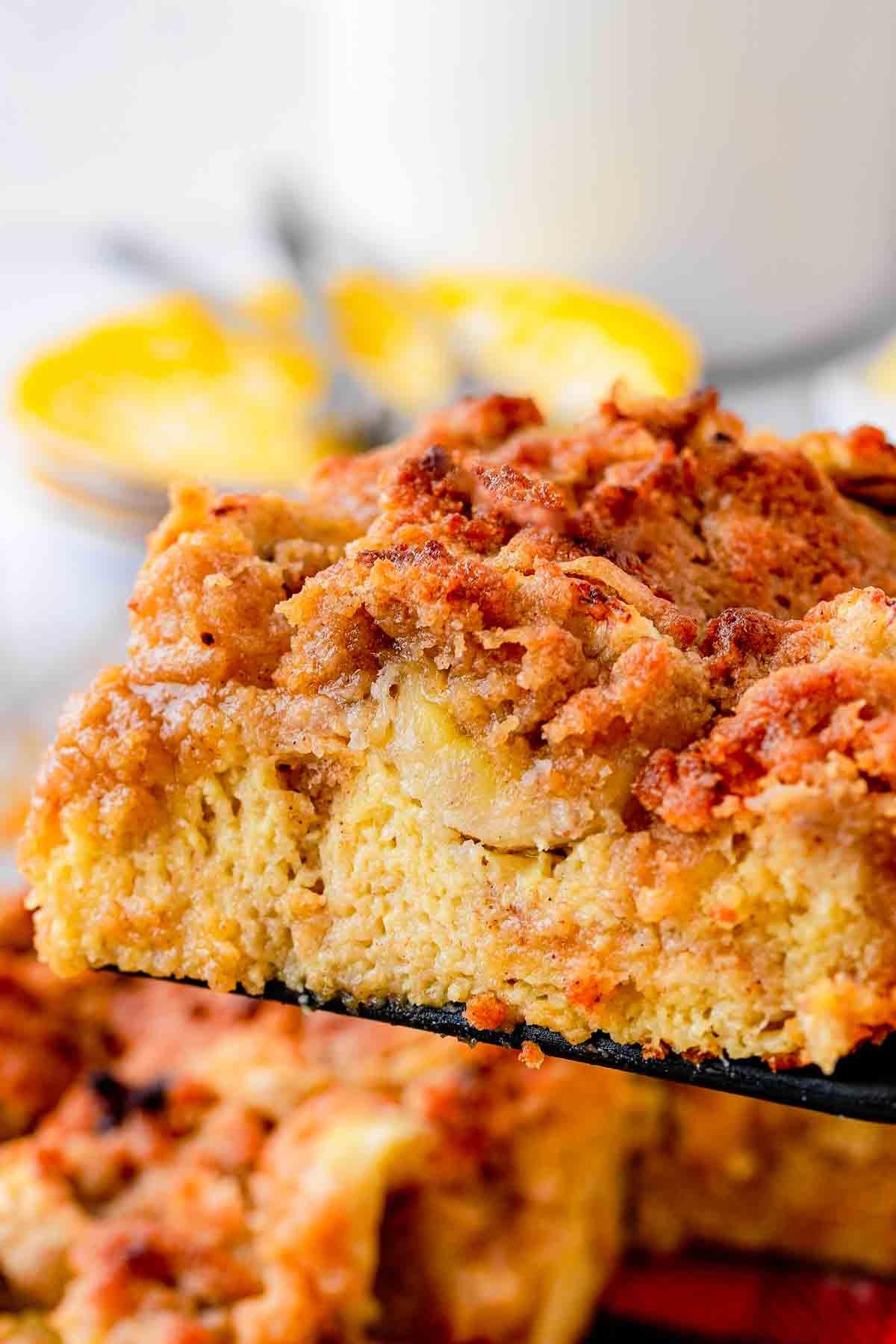 A slice of Banana French Toast Casserole on spatula with streusel topping and syrup poured on top