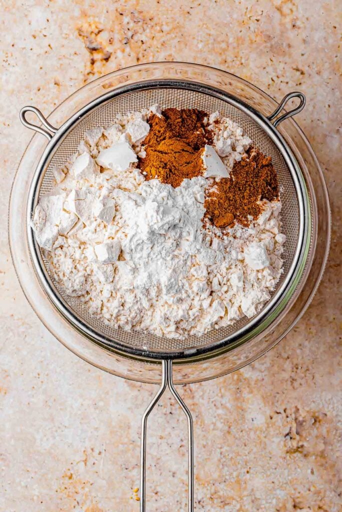 twice sifter flour, nutmeg, baking soda, salt and cinnamon in the bowl inside the sifter