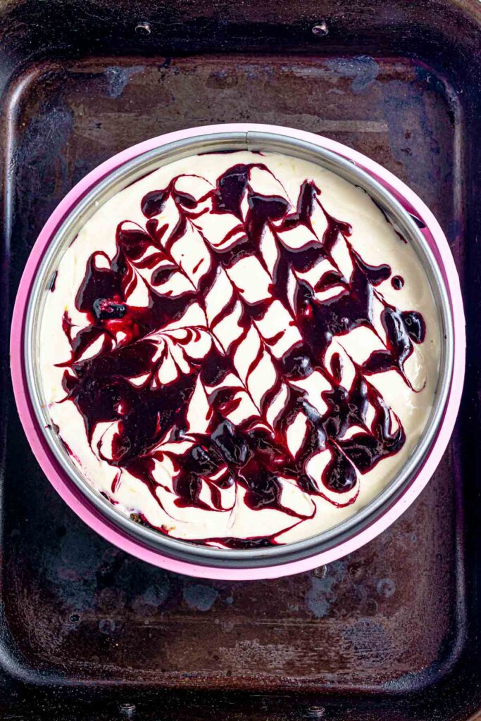 making precise blueberry swirls on top of a lemon cheesecake