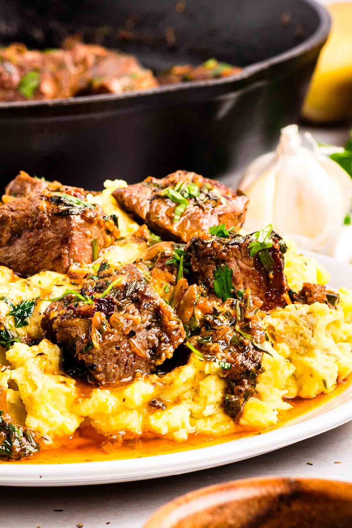 Garlic butter steak bites in a cast iron skillet, coated in herb compound butter sauce with garlic, parsley, and chives