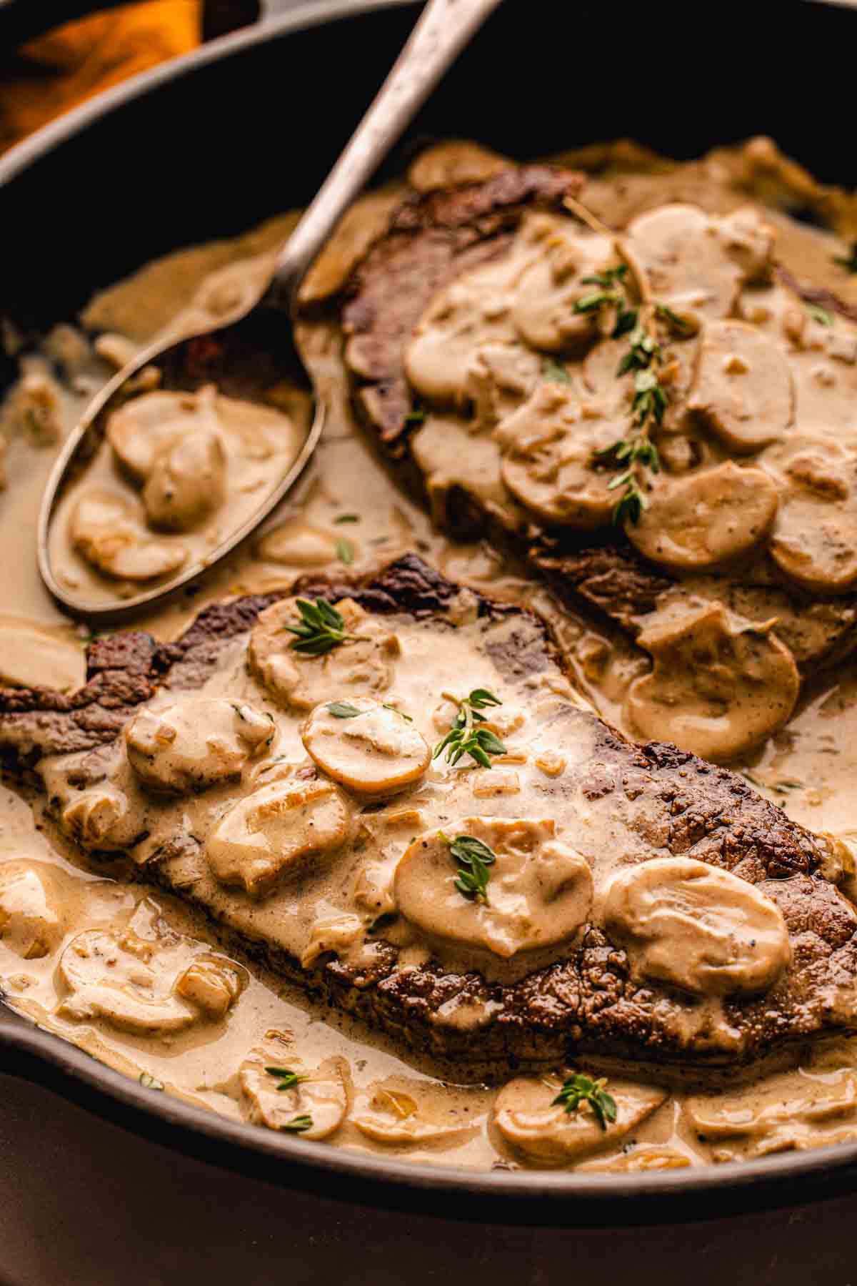Cast-iron skillet filled with Steak Diane: seared beef tenderloin medallions nestled in a creamy mushroom cognac sauce with fresh thyme sprigs