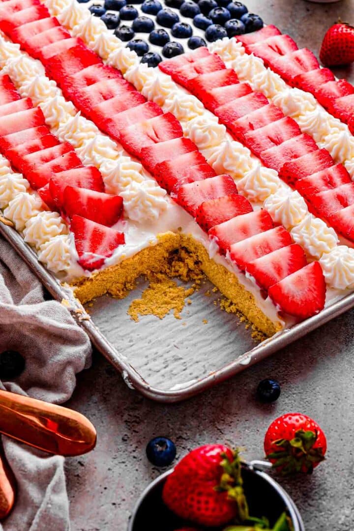 American Flag Fruit Pizza on a wooden board with a few slices removed, arranged on a picnic-style table for a patriotic Memorial Day or 4th of July gathering.