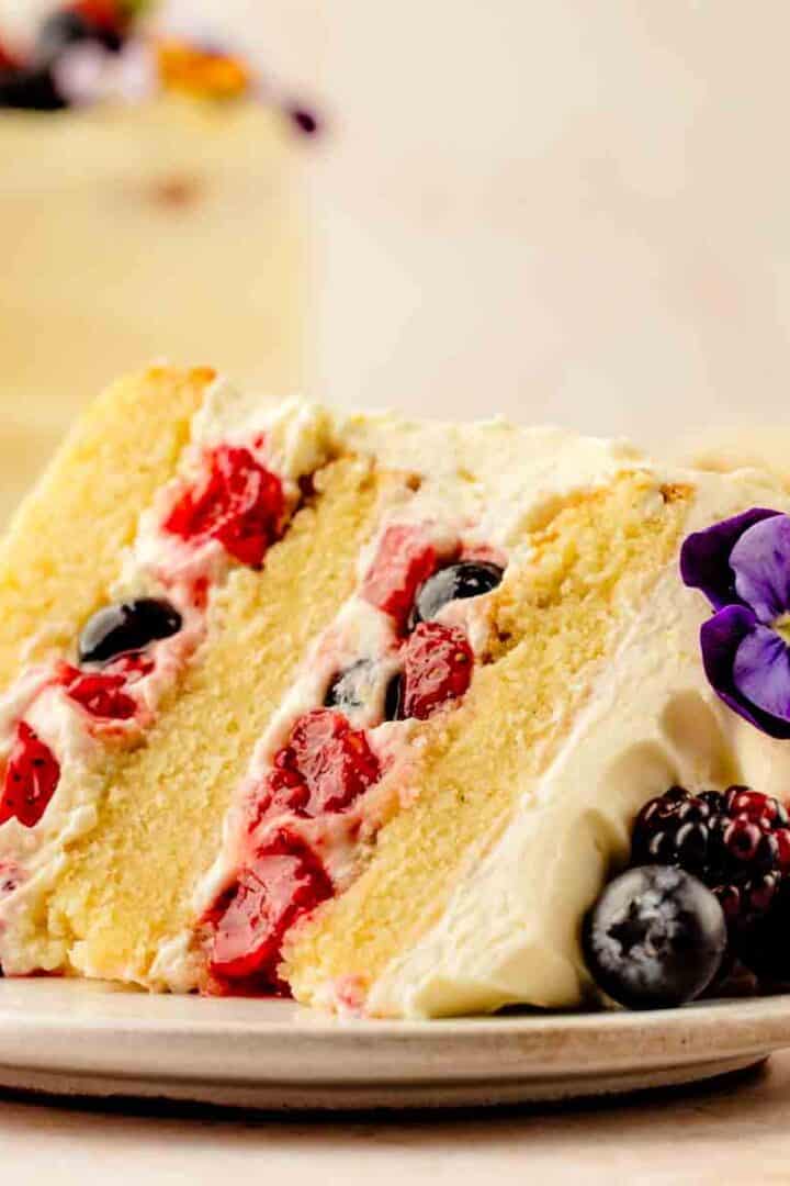 Berry Chantilly Cake on cake stand with mascarpone frosting, fresh strawberries, raspberries, and blueberries on top. Overhead whole cake: Overhead view of Berry Chantilly Cake decorated with mixed fresh berries and edible flowers.