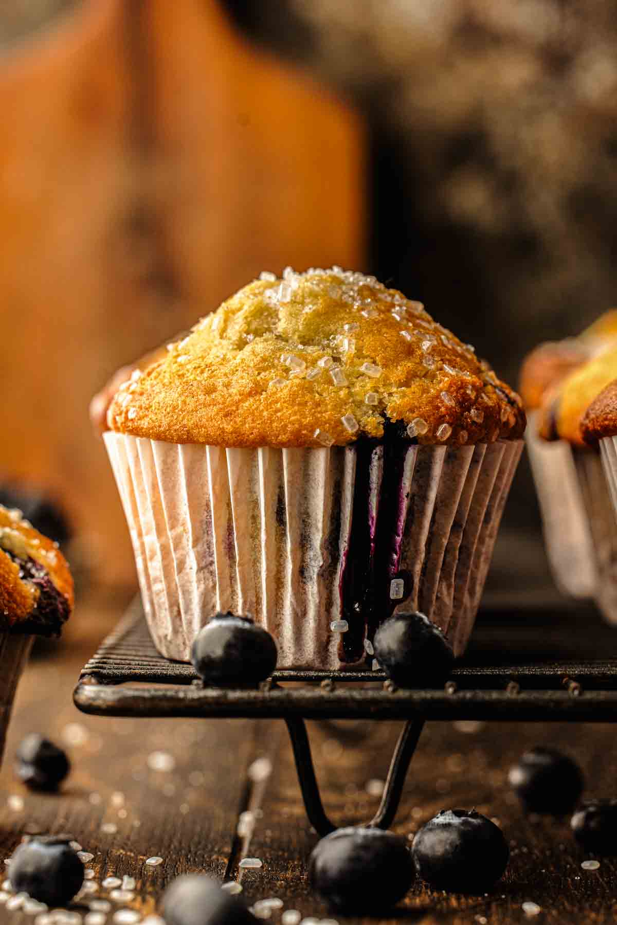 Freshly baked blueberry muffins with crunchy sugar tops in a muffin pan lined with white paper liners
