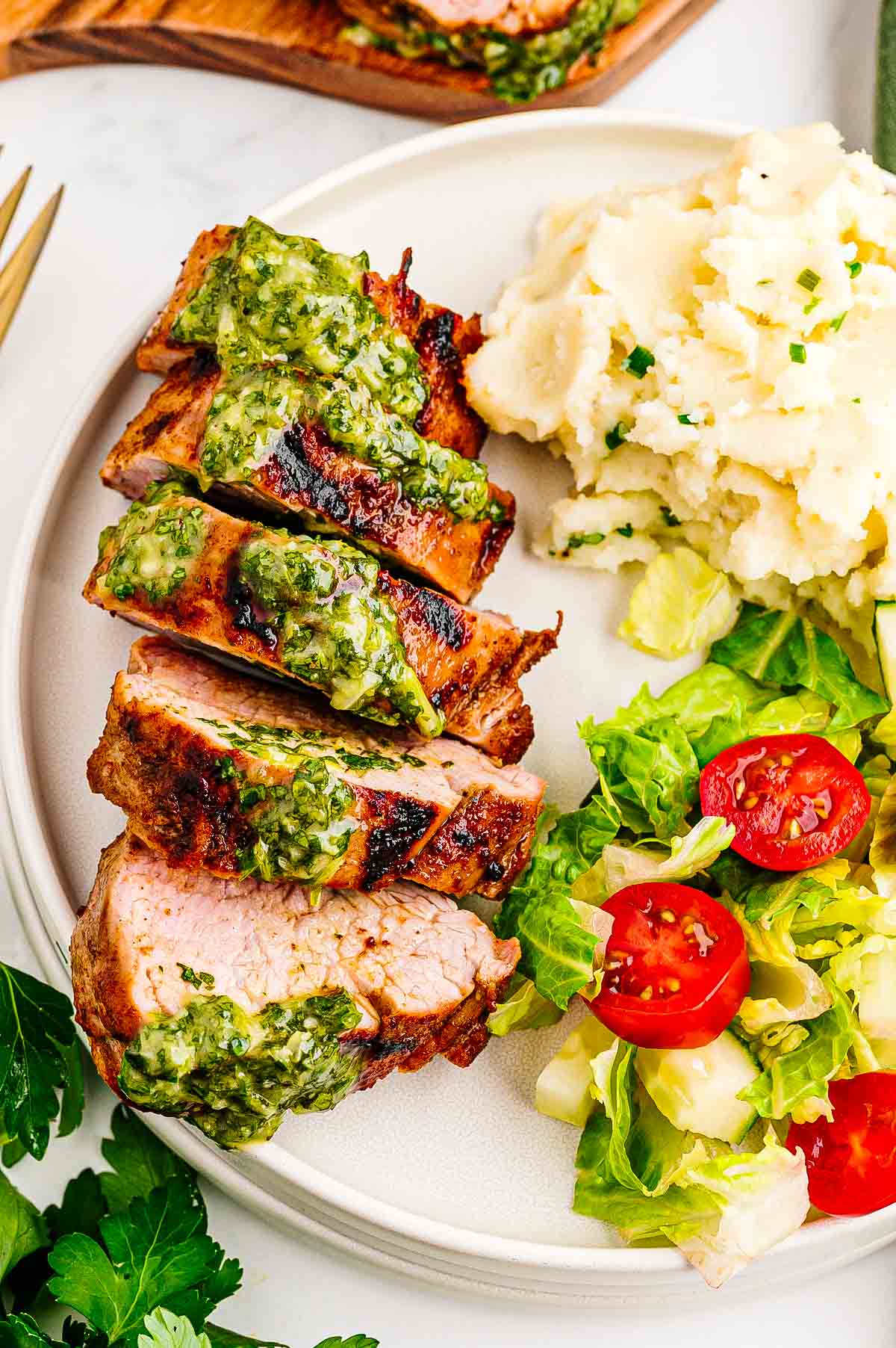 Close-up of juicy grilled pork tenderloin slices showing a slight pink center with herb sauce drizzled on top.