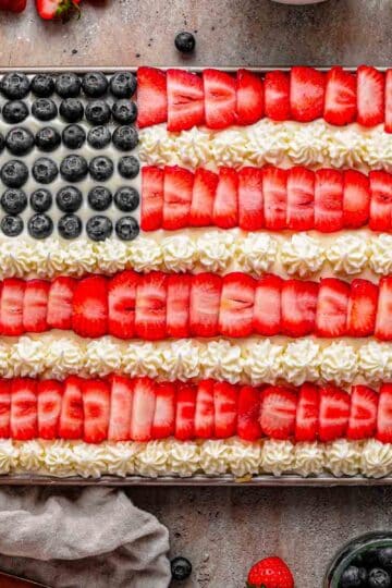 American Flag Fruit Pizza in a rectangular pan, topped with neat rows of strawberries and blueberries and piped white frosting stripes, ready to slice for a summer party.