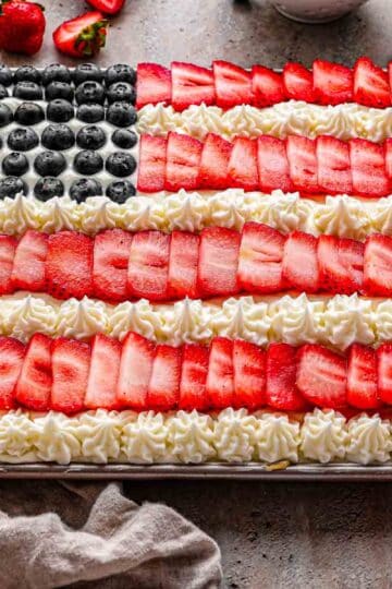 American Flag Fruit Pizza in a rectangular pan, topped with neat rows of strawberries and blueberries and piped white frosting stripes, ready to slice for a summer party.