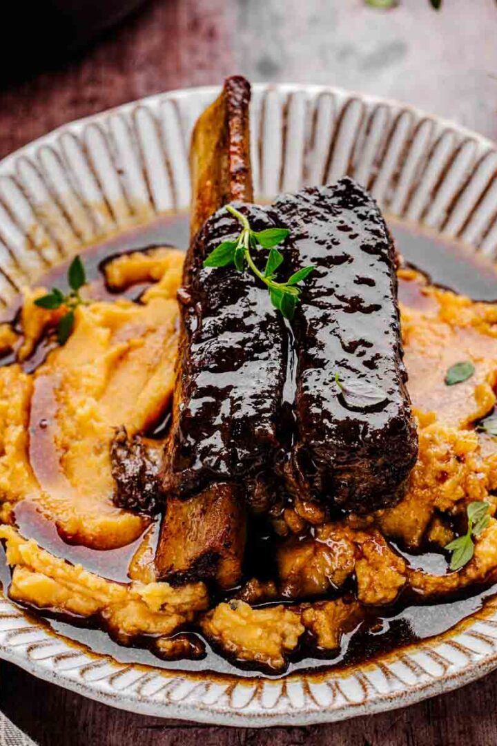 Restaurant-style red wine braised short ribs with mashed potatoes and fresh thyme, showing tender meat and reduced sauce.