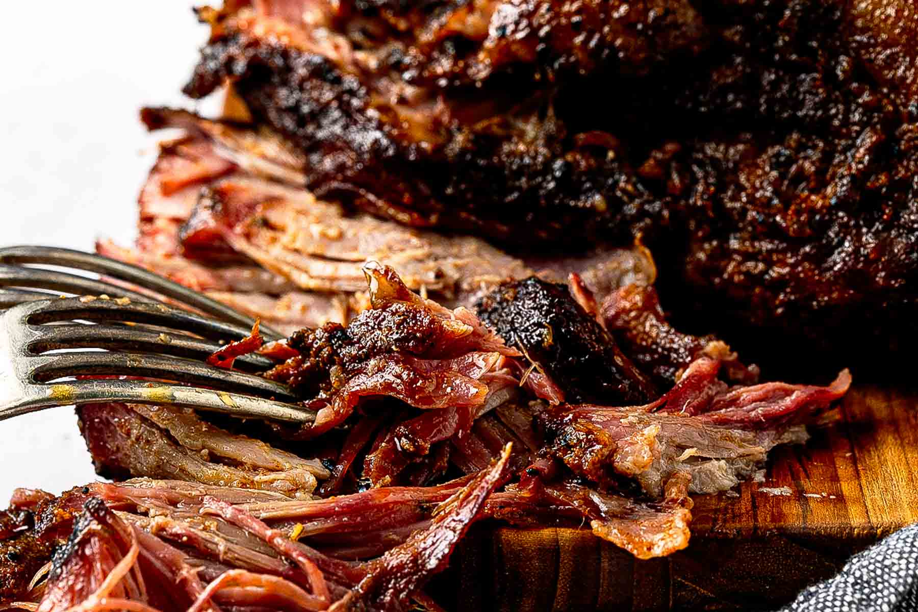 Smoked Boston shoulder pulled apart into tender shreds on a wooden cutting board with bark pieces and cooking juices