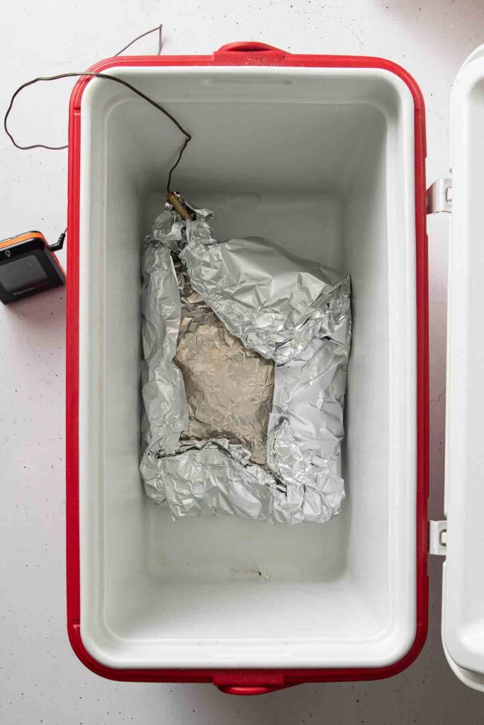 Cooler with wrapped pork butt and folded kitchen towels on top to hold heat during resting period