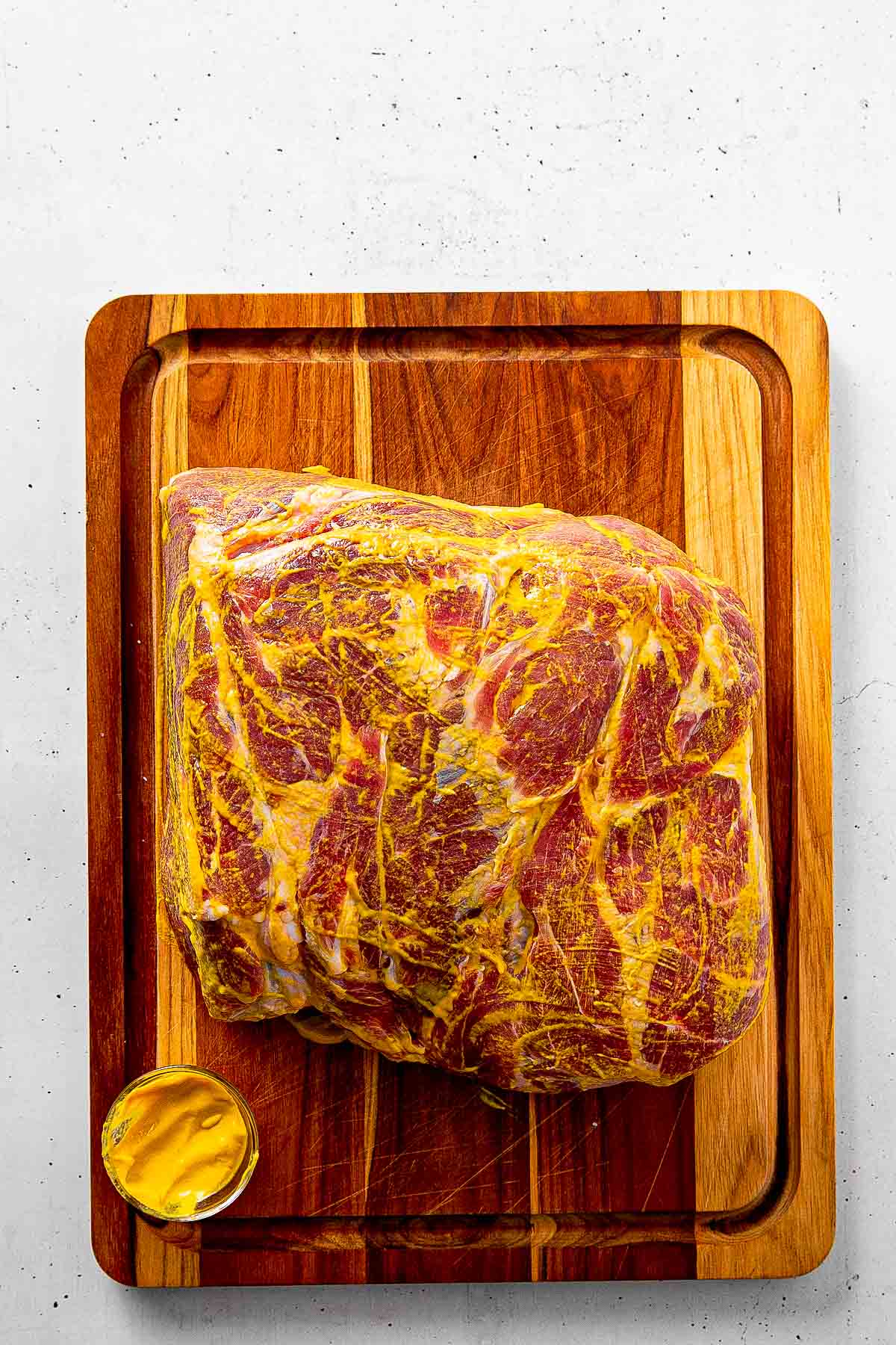 Spreading yellow mustard binder over a Boston butt with hands before applying dry rub