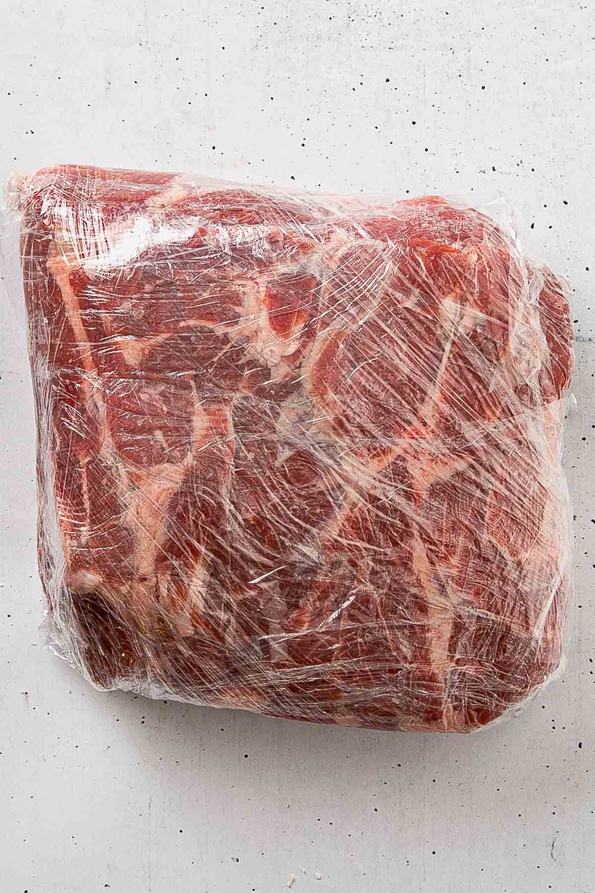 Pork butt wrapped tightly in plastic wrap for overnight dry brine in the refrigerator