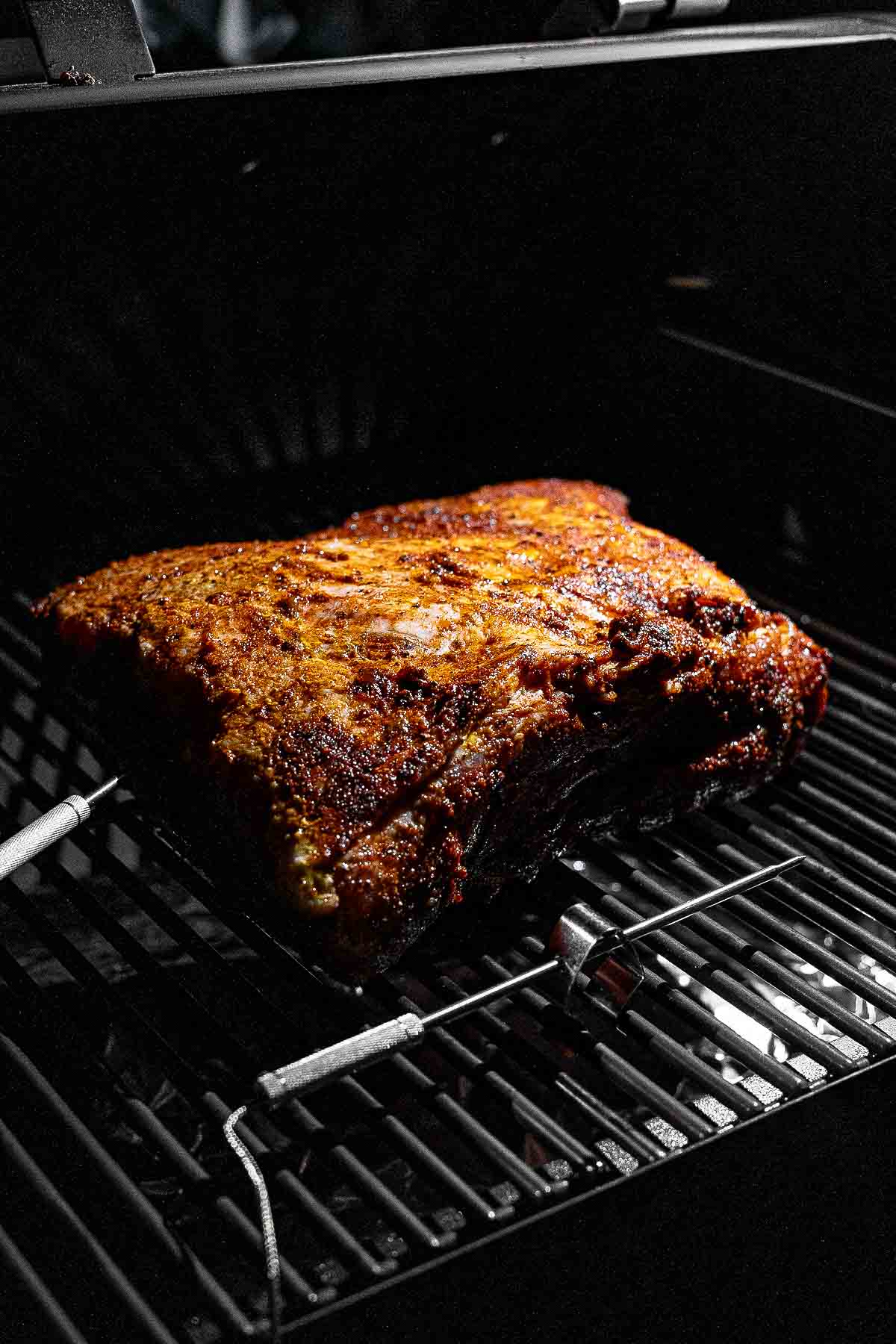 Leave-in digital meat thermometer probe inserted into the thickest part of a pork butt on the smoker