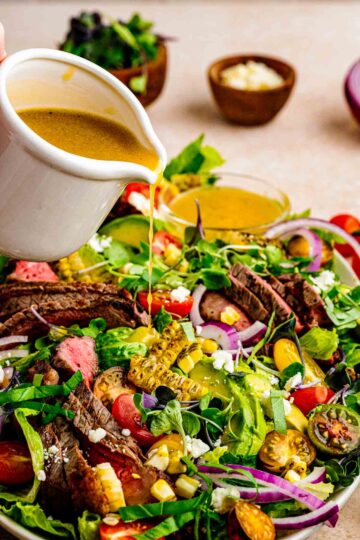 steak and salad with dressing being poured on top of it