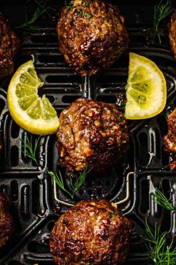 Overhead shot of air fryer lemon herb meatballs with whipped feta dip, lemon wedges, and fresh herbs in the air fryer