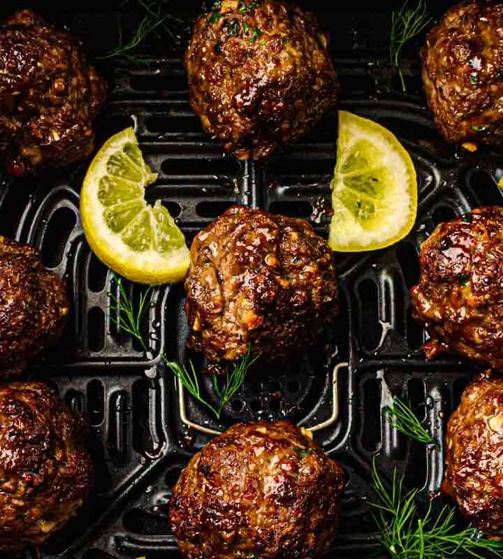 Overhead shot of air fryer lemon herb meatballs with whipped feta dip, lemon wedges, and fresh herbs in the air fryer