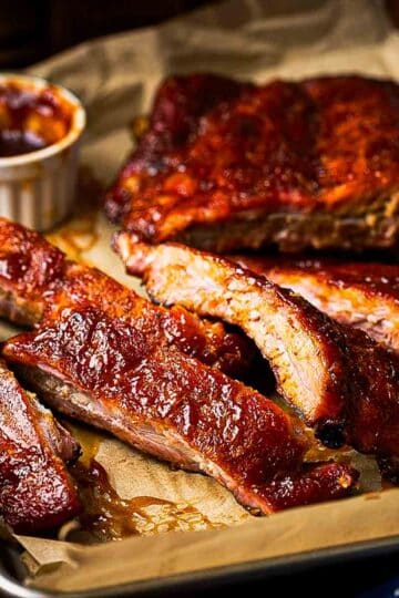 Plated smoked baby back ribs with coleslaw and corn on the cob on a rustic wood table with condensation on a cold lager in the background