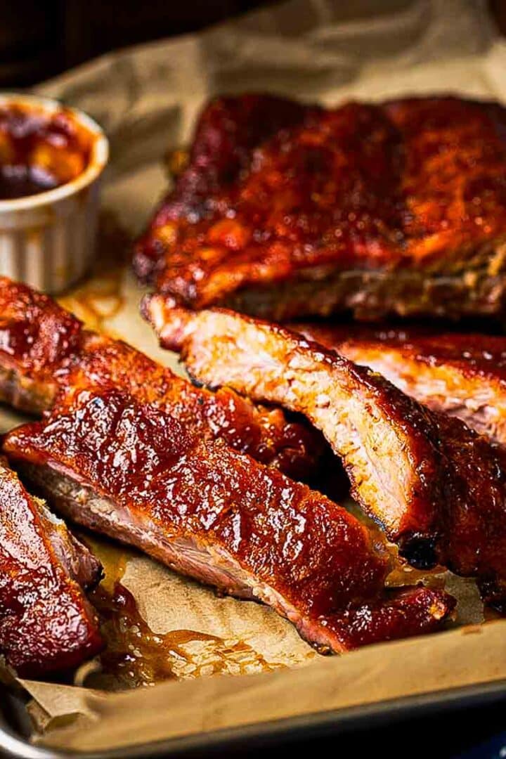 Plated smoked baby back ribs with coleslaw and corn on the cob on a rustic wood table with condensation on a cold lager in the background