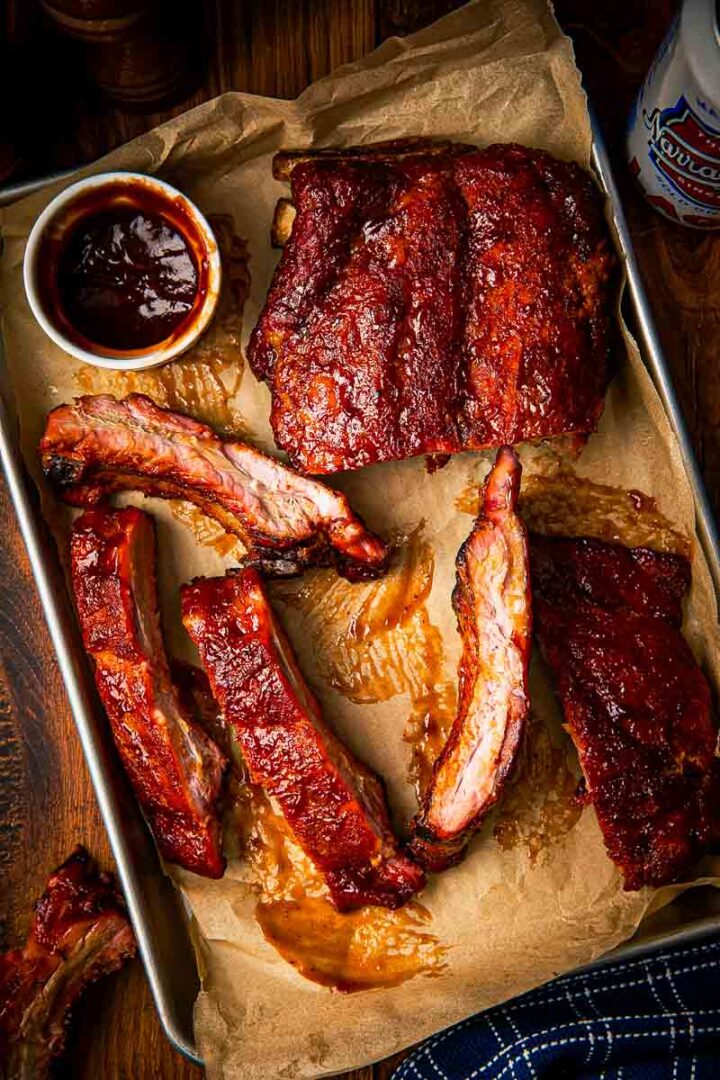 Whole rack of 3-2-1 smoked baby back ribs fresh off the smoker resting on a wire rack over a sheet pan with juices pooling underneath
