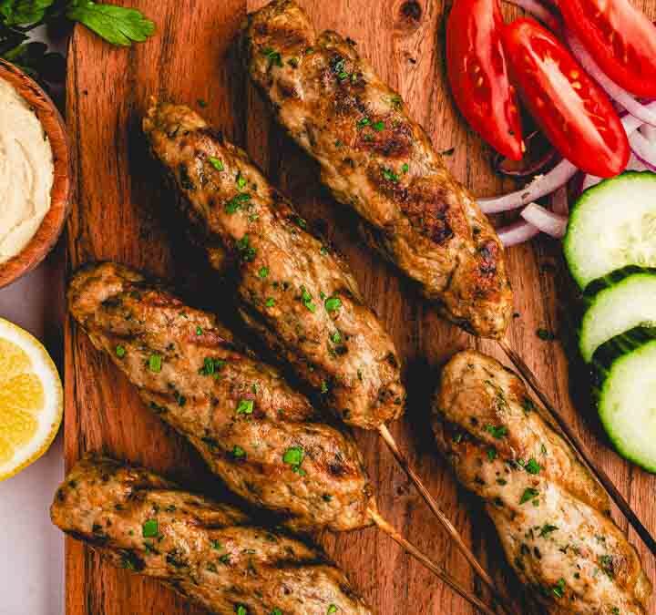 Chicken kofta skewers plated on a bed of yellow rice with tzatziki, warm pita triangles, and fresh parsley on a rustic wood table