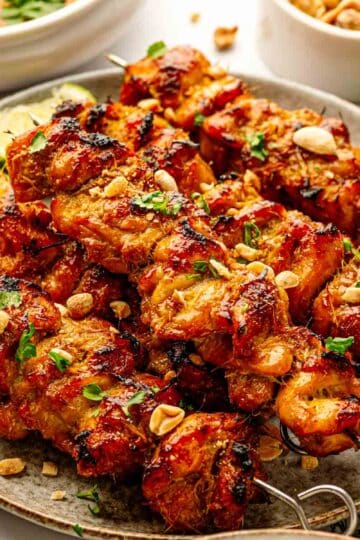 Oven-baked Thai chicken satay skewers on a wire rack served over jasmine rice with coconut peanut sauce and lime wedges