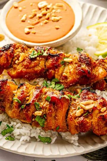 Thai chicken satay skewers on a wire rack with visible caramelized marinade, served with jasmine rice and peanut sauce
