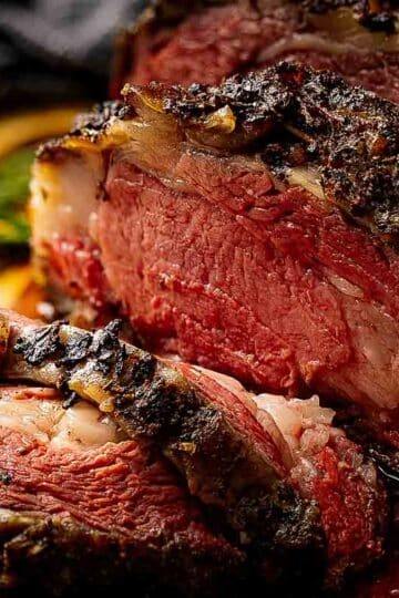Sliced smoked prime rib showing pink medium-rare center and dark coffee bark on a wooden cutting board