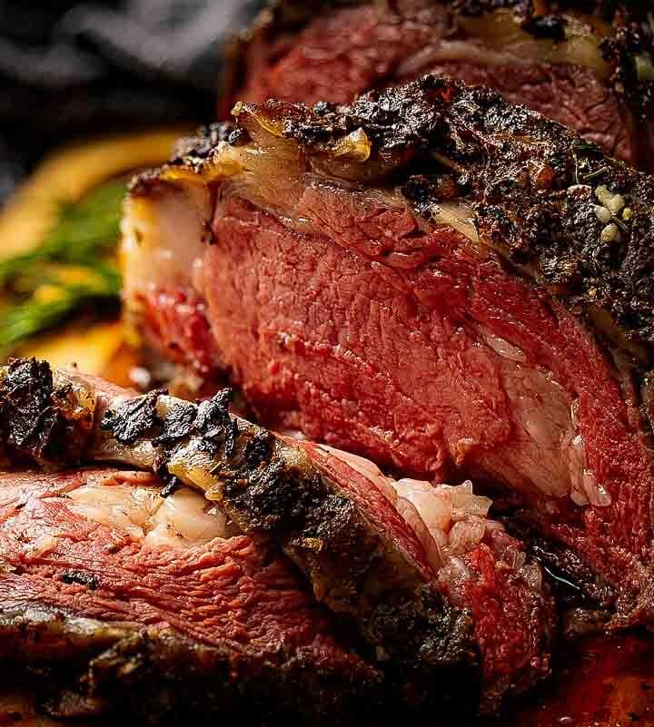 Sliced smoked prime rib showing pink medium-rare center and dark coffee bark on a wooden cutting board