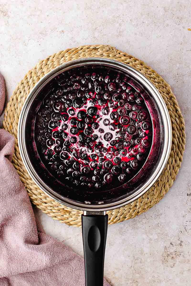 Frozen blueberries and sugar cooking down in a saucepan over medium heat for homemade cake filling"