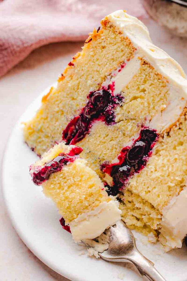 Cut vanilla blueberry layer cake revealing thick homemade blueberry filling and three soft vanilla cake layers