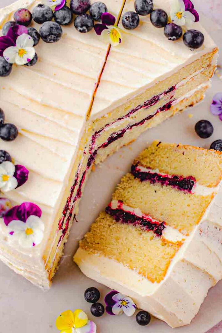 A slice of vanilla blueberry layer cake laying on the white surface with blueberry filling and vanilla buttercream showing between the layers