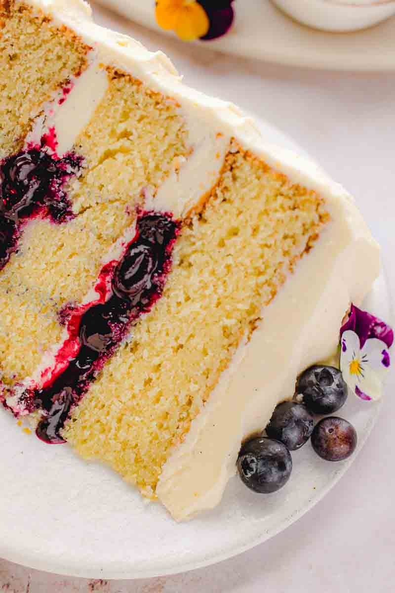 Three-layer vanilla blueberry cake sliced to show thick homemade blueberry filling and vanilla bean buttercream