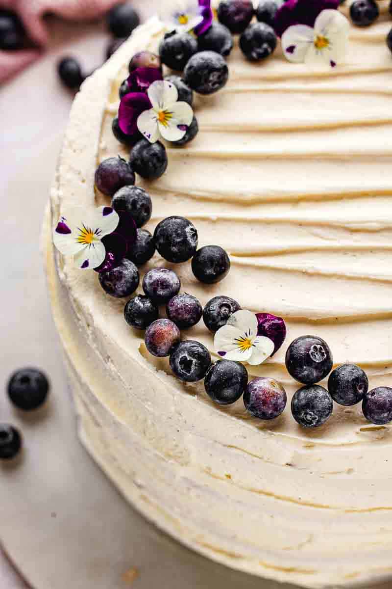 "Overhead shot of vanilla blueberry layer cake decorated with fresh blueberries on a white cake board"