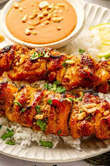Oven-baked Thai chicken satay skewers on a wire rack served over jasmine rice with coconut peanut sauce and lime wedges