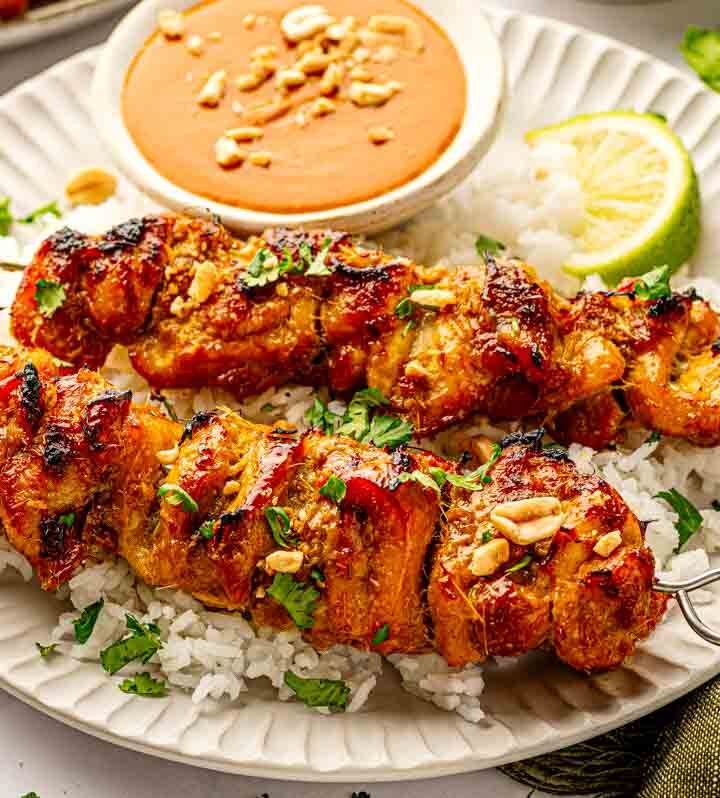 Oven-baked Thai chicken satay skewers on a wire rack served over jasmine rice with coconut peanut sauce and lime wedges