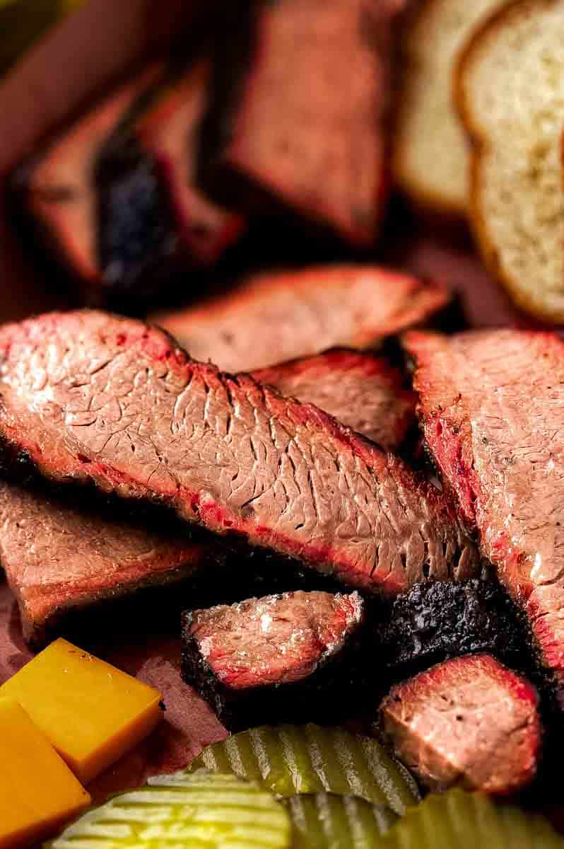 Close-up of a hand slicing a rested brisket flat against the grain with a sharp carving knife.