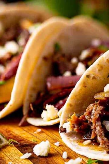 Close-up of Tex-Mex pulled beef street taco showing juicy shredded beef, pink pickled red onions, crumbled cotija, and charred tortilla edges.