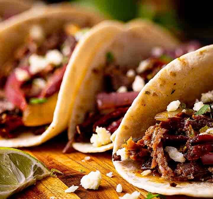 Close-up of Tex-Mex pulled beef street taco showing juicy shredded beef, pink pickled red onions, crumbled cotija, and charred tortilla edges.