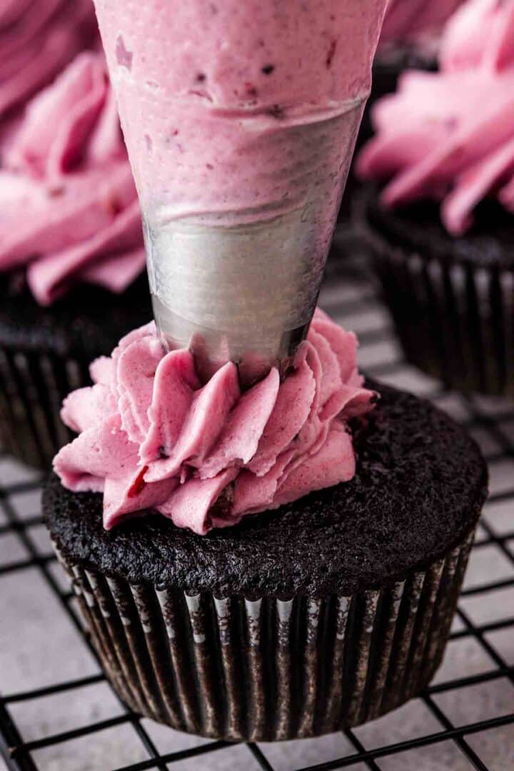 Blackberry buttercream frosting made with chopped blackberries being piped on top of chocolate cupcake