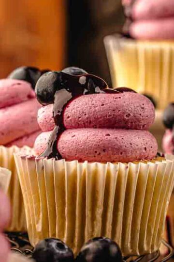 Lemon blueberry cupcakes styled on a wooden board with lemons and blueberries scattered nearby.
