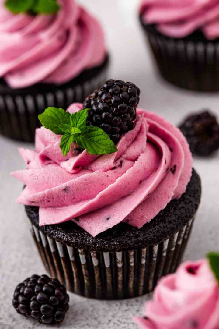 Close-up of dark chocolate blackberry cupcakes topped with blackberry frosting and fresh blackberries.