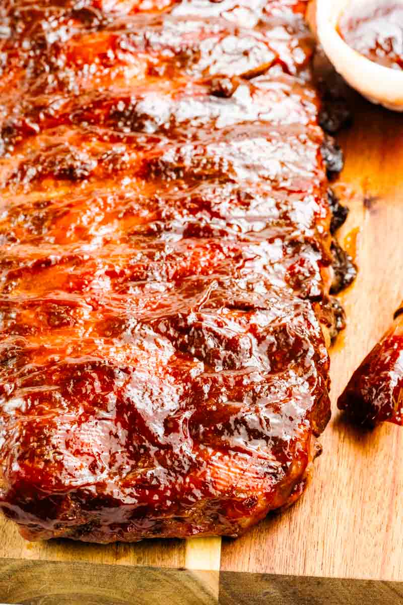 A close-up of juicy, glazed barbecue ribs garnished with chopped green onions, arranged on a white surface with a jar of barbecue sauce in the background.
