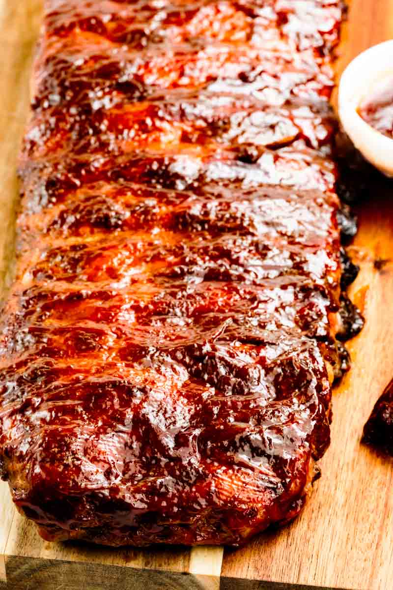 Whole rack of grilled BBQ ribs on a gas grill over indirect heat, with caramelized BBQ sauce and light char marks, demonstrating the 2-step foil-and-grill method
