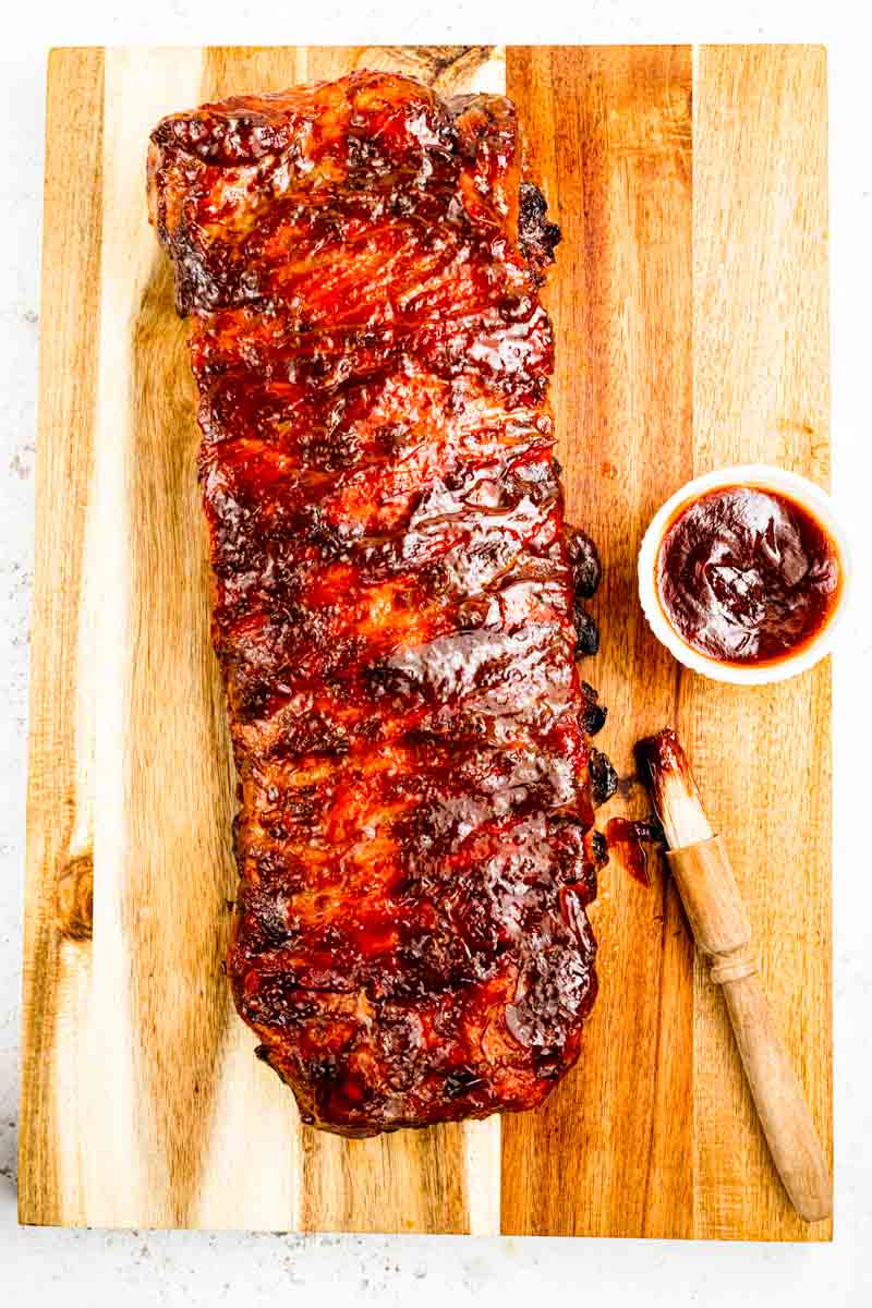 Whole rack of grilled BBQ ribs on a gas grill over indirect heat, with caramelized BBQ sauce and light char marks, demonstrating the 2-step foil-and-grill method