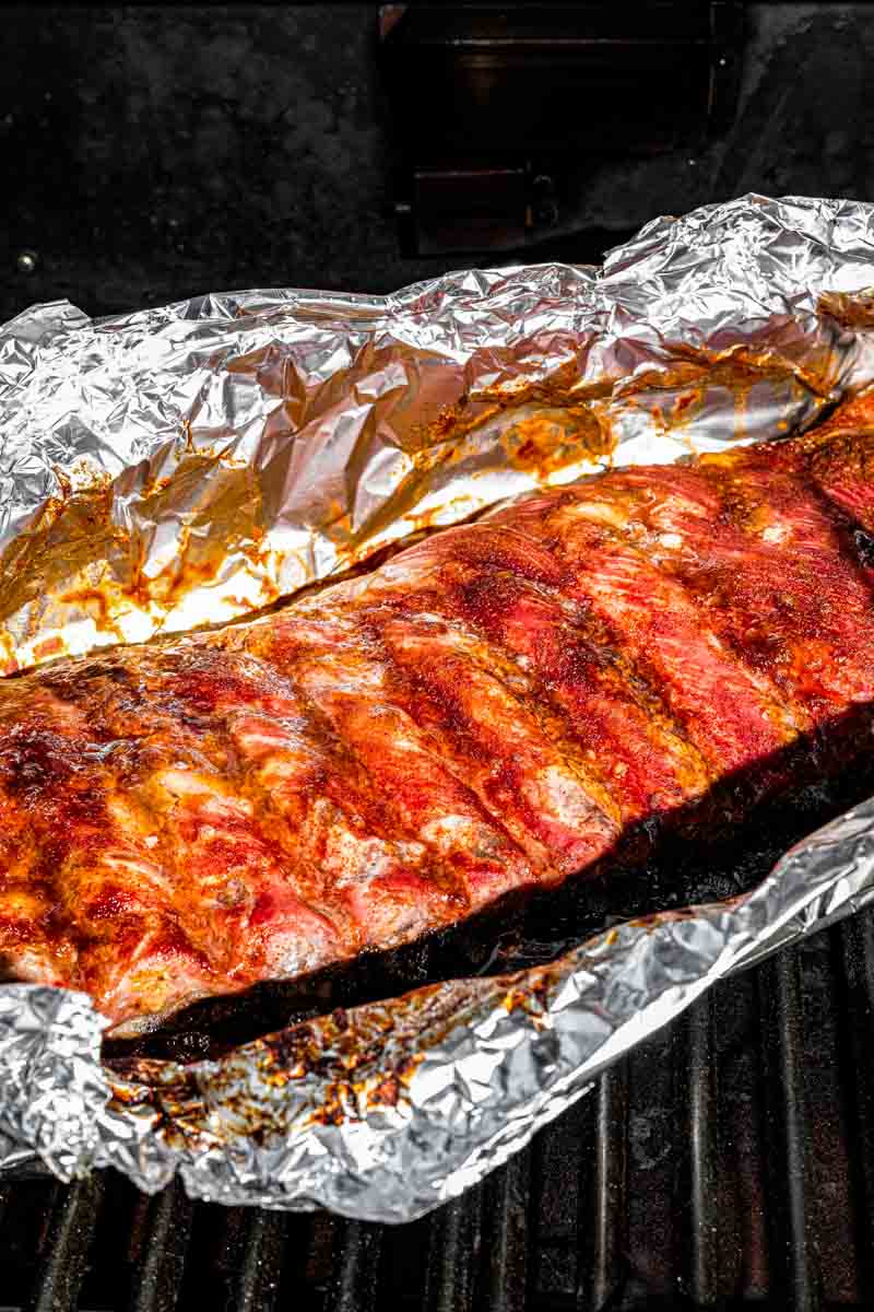 Ribs in foil on the barbecue grill with BBQ sauce on top ready to be grilled