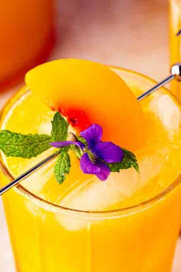 Hero shot of a hand holding a glass of peach ginger mocktail over a tray of more mocktails, emphasizing party serving.