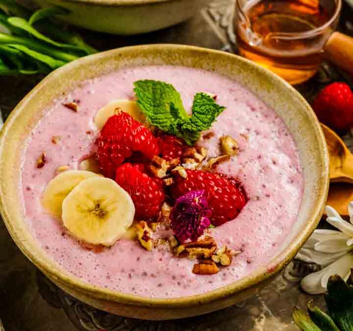 Hero image of raspberry chia pudding surrounded by ingredients-coconut milk, raspberries, chia seeds-suggesting a simple dairy-free recipe.