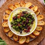Overhead shot of whipped feta and roasted olives surrounded by crispy baguette slices.