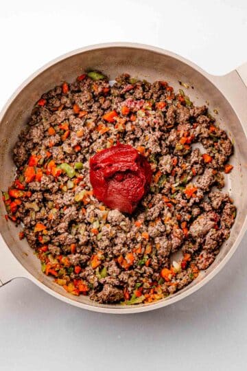 Tomato paste stirred into browned ground beef, darkening in the pot to build deeper flavor